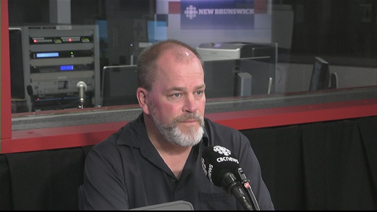 A man sits in front of a CBC microphone in a news booth.