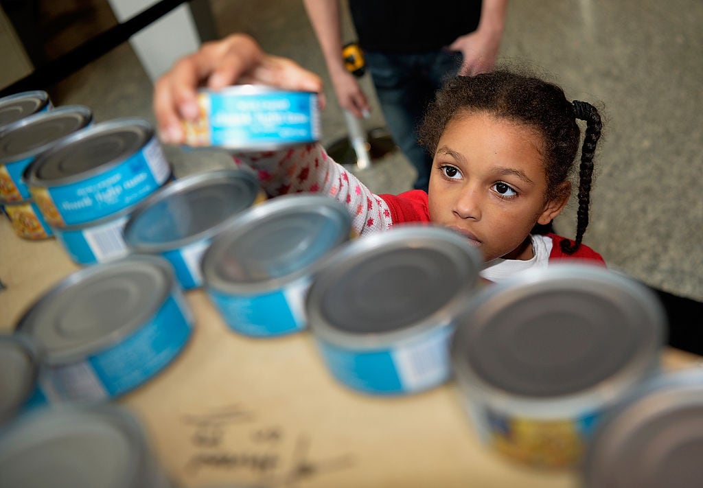 Girl picks up a can of tuna from a shelf