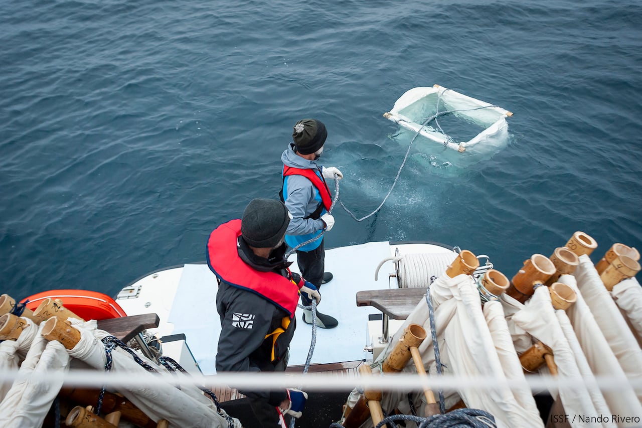 Man with a rope attached to a floating rectangle in the water, with others stacked on the boat