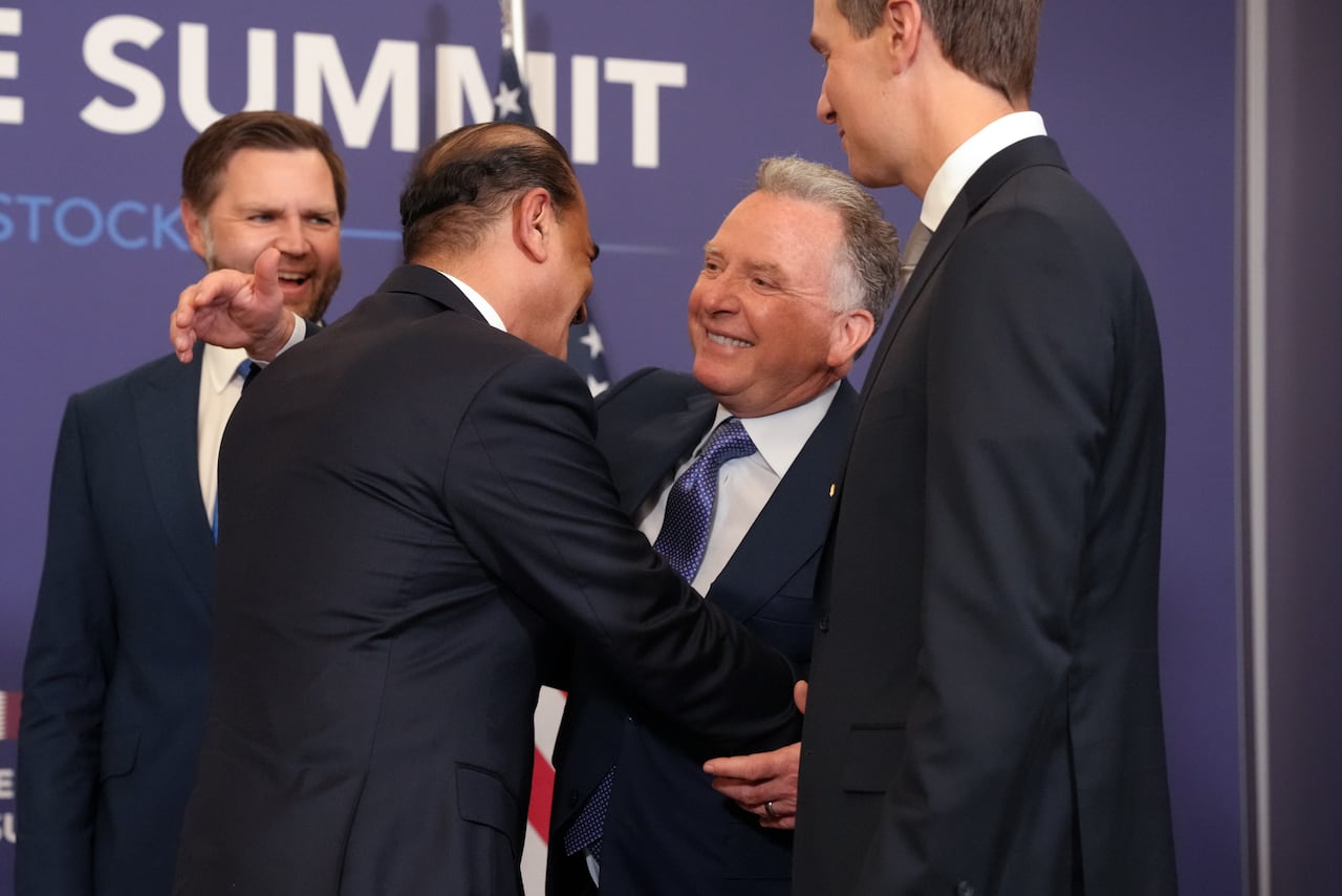 Two men in suits hug as two other men in suits look on, smiling.