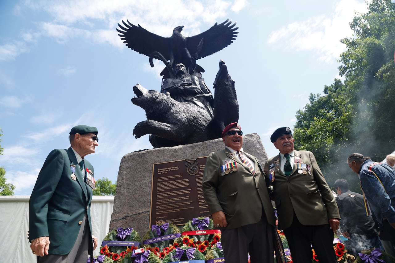 Three men in uniform stand in front of a monument topped by a bird.