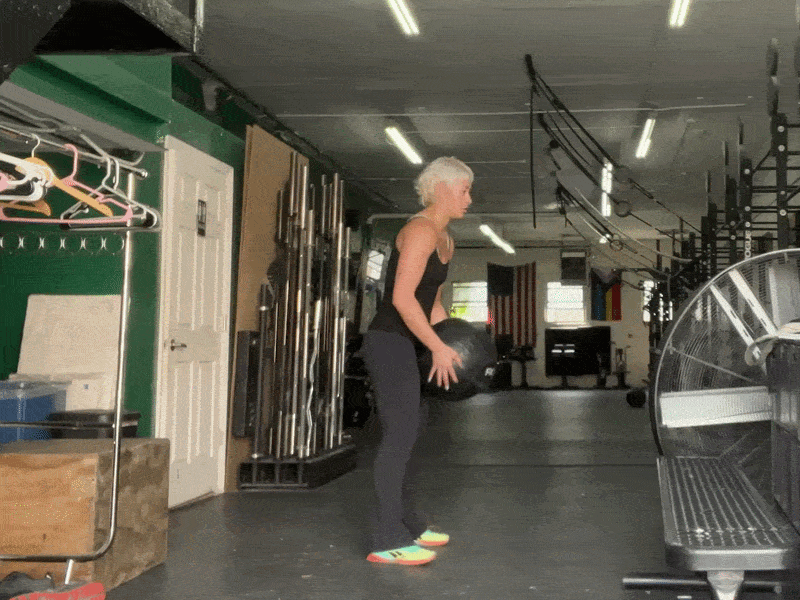 This is a photographic GIF showing the medicine ball slam exercise. In this exercise, raise a medicine ball above your head with both hands, and then forcefully slam it straight down to the ground.