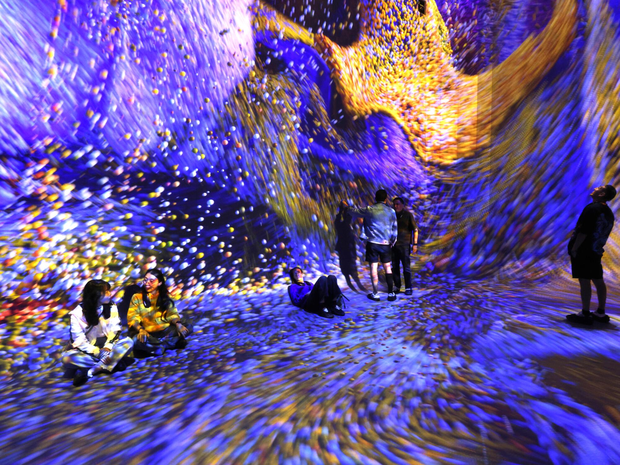 People sit and stand in a room surrounded by swirling purple lights 