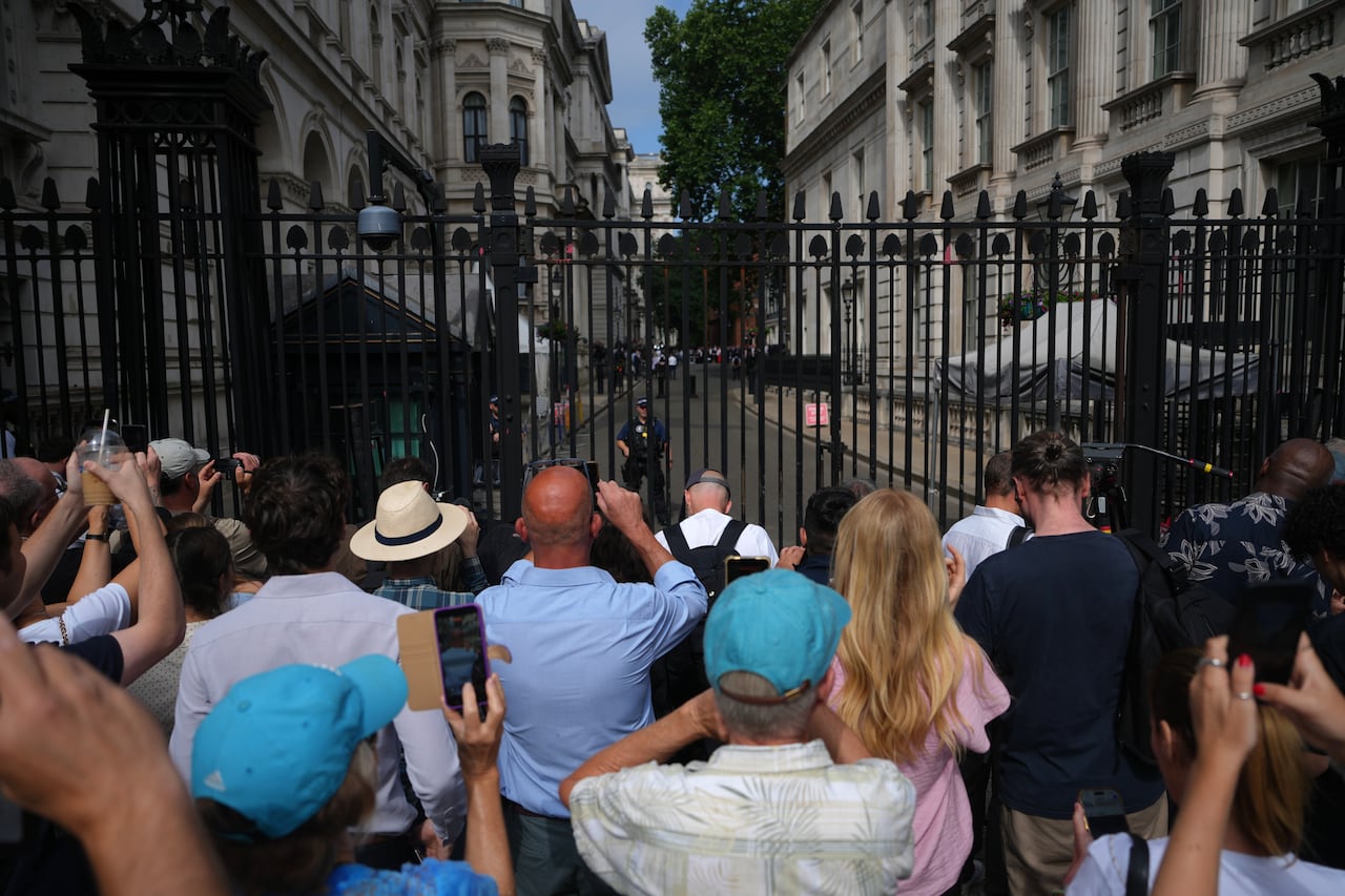 A couple dozen people, with backs to camera, are shown crowded near a fence.