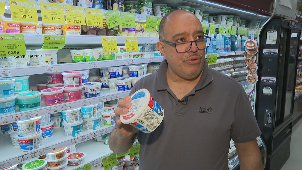 A man holds up a product in front of a grocery store cooler.