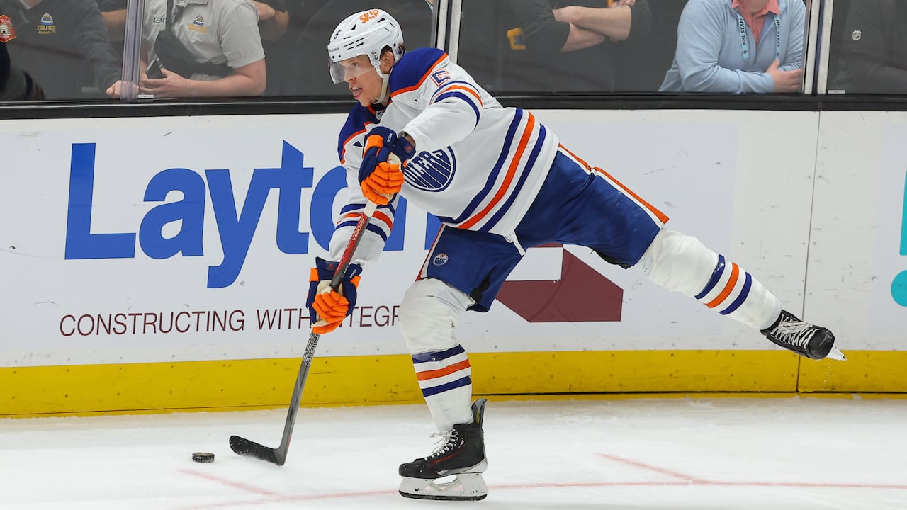 A hockey player in a white jersey with blue trim shoots the puck.