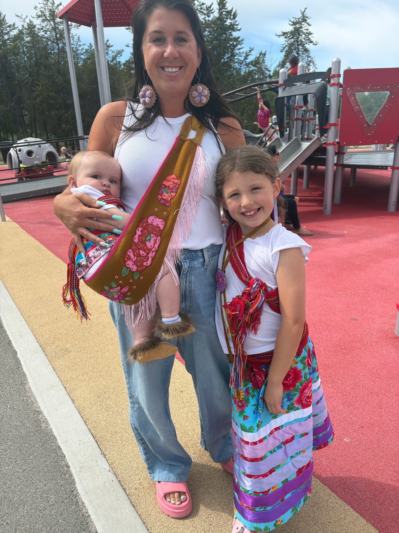 Winter Harmon, six-months, Emily Harmon and River Harmon, 7, arrived at the annual North Slave Métis Alliance's Indigenous Peoples Day celebrations decked out in ribbon skirts, Métis sashes and beadwork. Winter's sling was made by Janet Bishop.