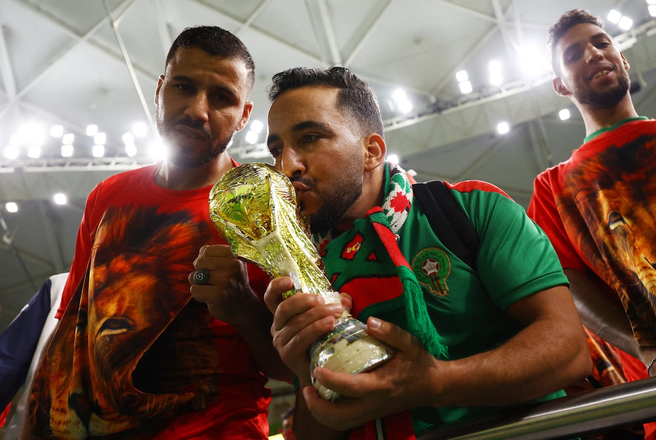 A man in a Moroccan jersey kisses a replica of the FIFA World Cup.
