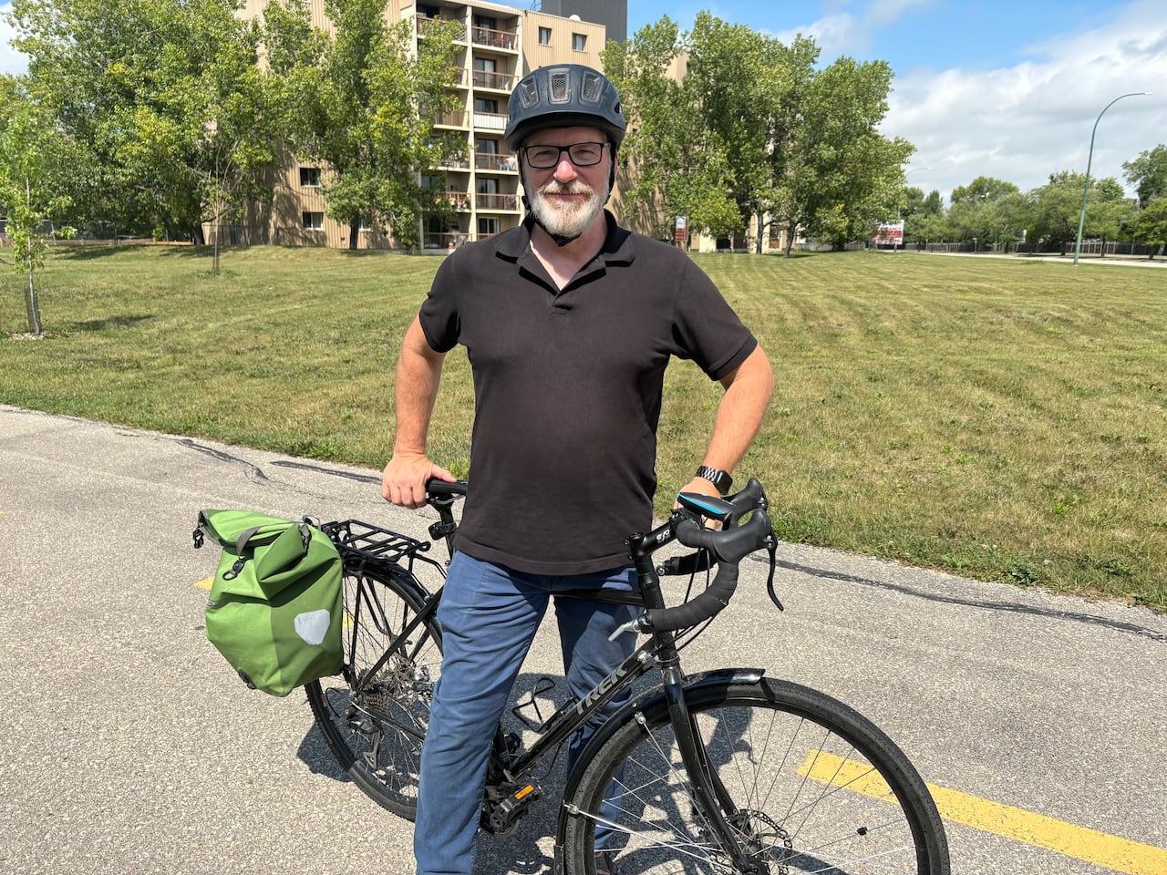 A man in a black shirt stands poses with a black bike. 