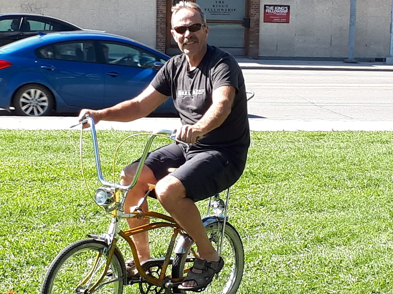 Man wearing sunglasses on a vintage-style bike with low-rider handlebars.