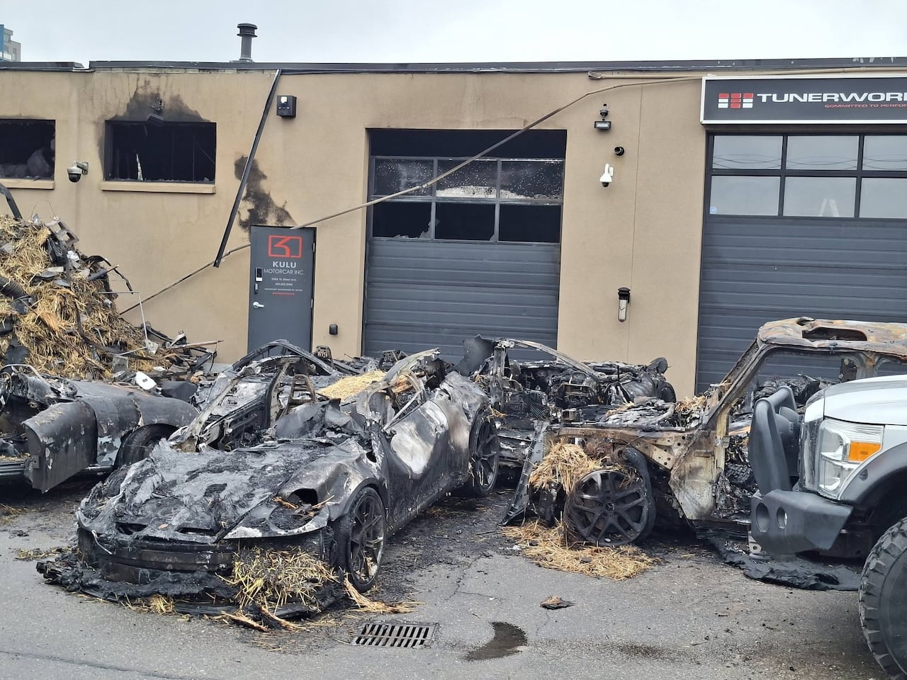 Burnt cars sit in front of a low building.
