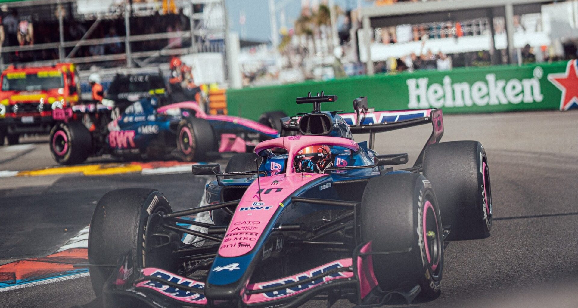 Front-right view of a pink Formula 1 car speeding on a race track with Heineken banners in the background.