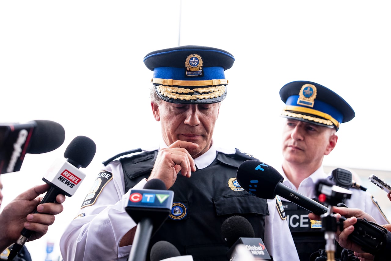 Two stoic police officers stand at a phanlanx of microphones. The microphones variously say Citynews, Rebel News, CTV, Global News and TVA.