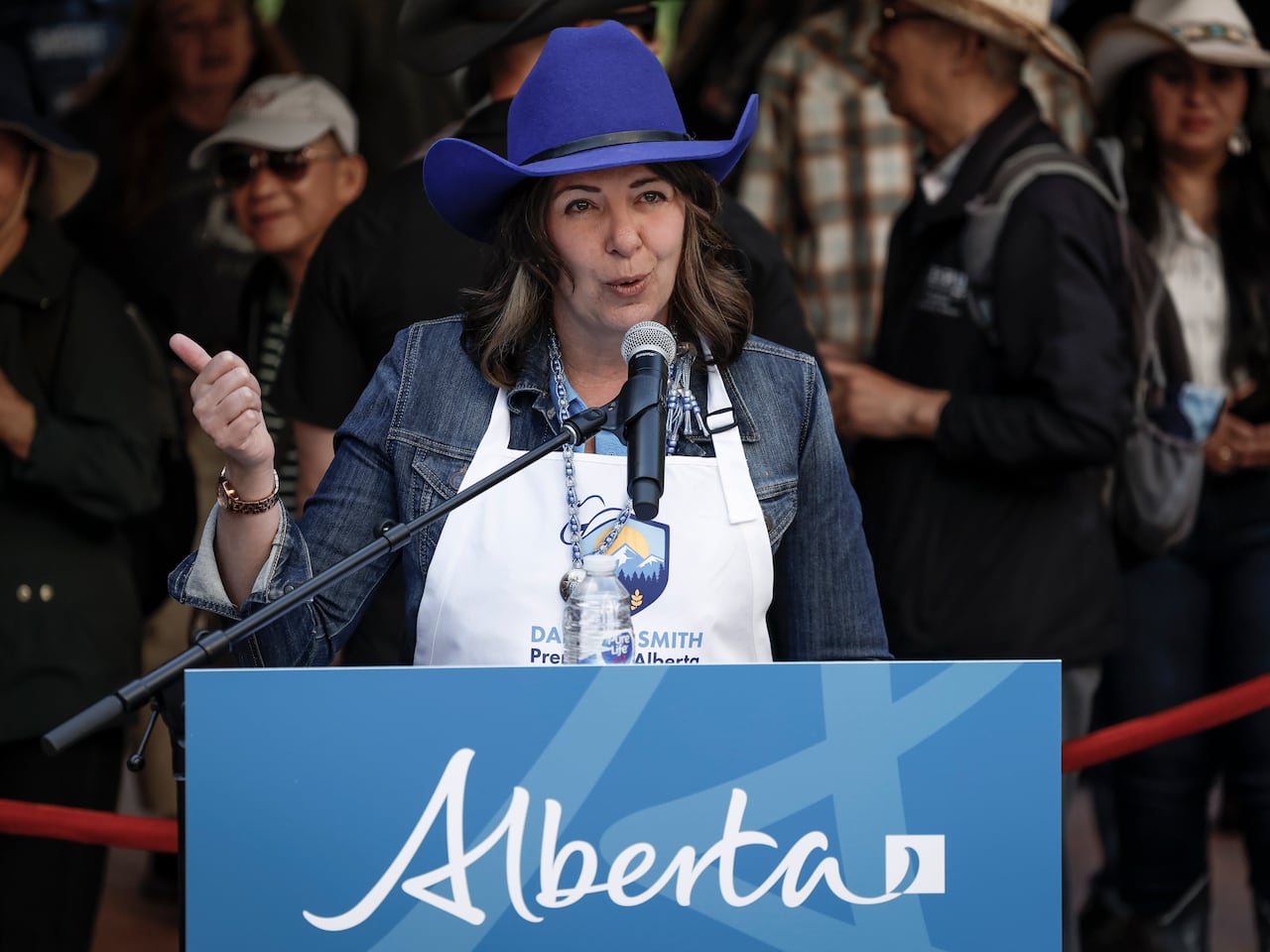 Woman in blue hat and apron points with her thumb as she talks into a microphone.