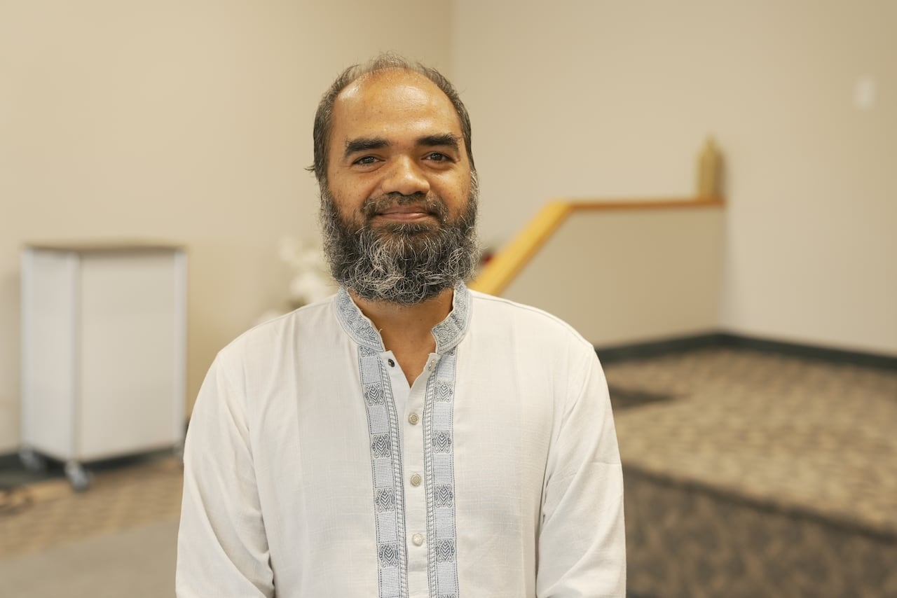 A man with a beard smiles for the camera in white, traditional Muslim clothing.