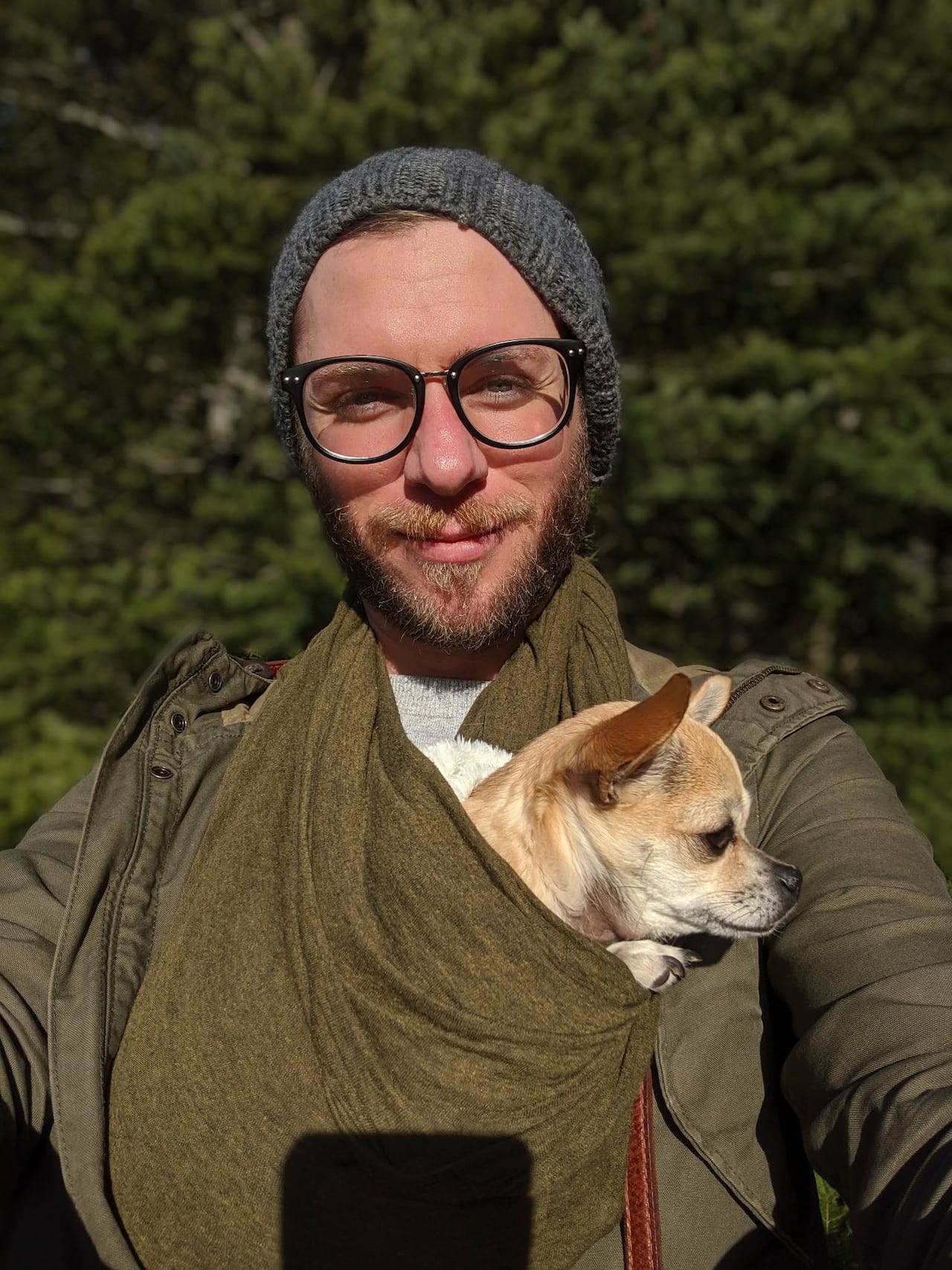 A man is pictured taking a selfie with a dog in a scarf pouch around his neck.