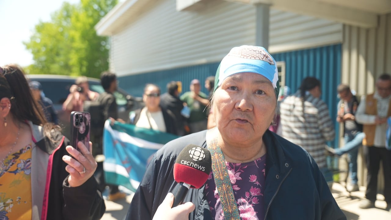 A woman faces the camera, a crowd is visible behind her.