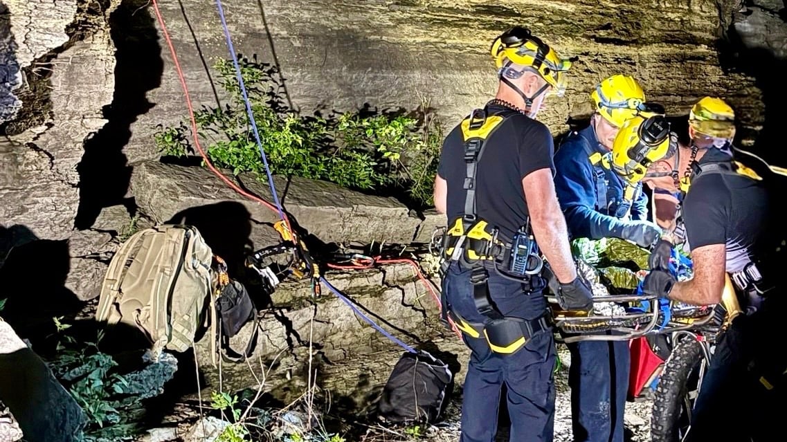 Firefighters work on a stretcher next to a cliff at night.