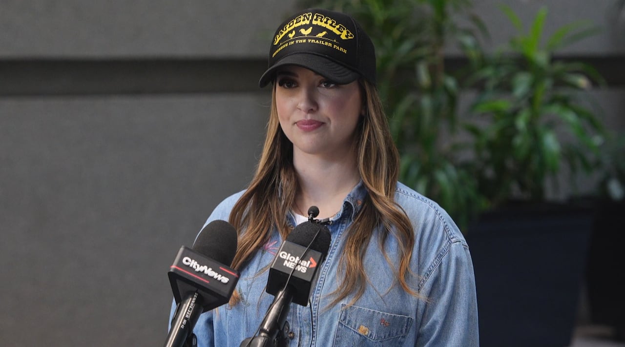 A woman wearing a baseball cap stands in front of a microphone.