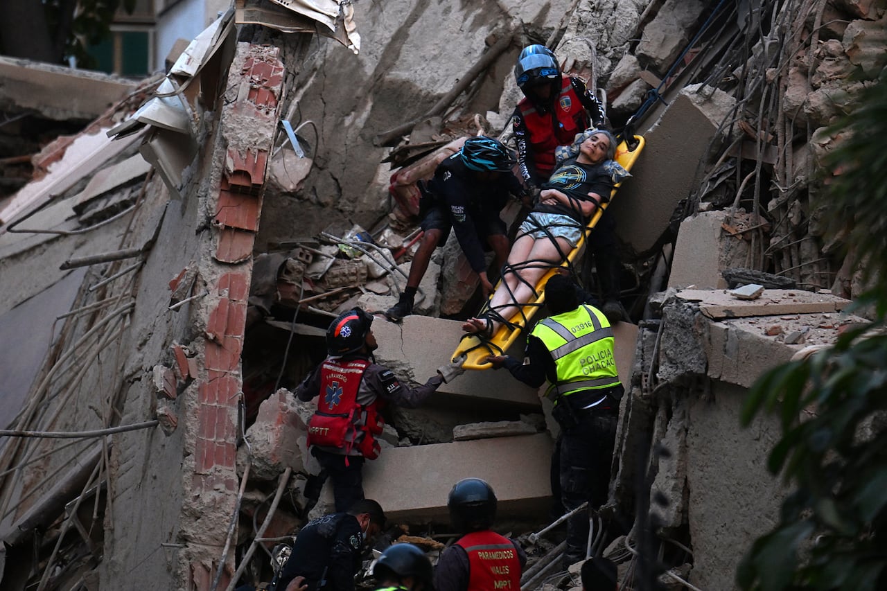A person on a backboard is helped out of a crumbled building with ropes