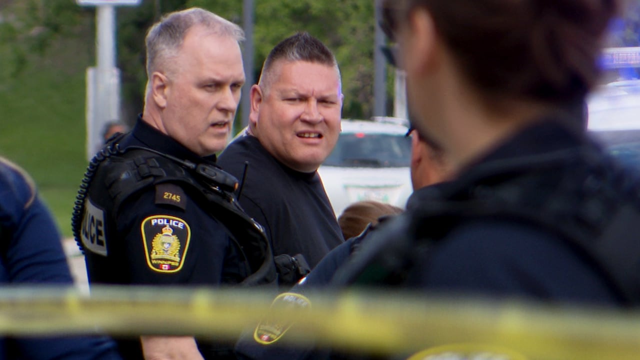 A man and a police officer standing by a police cruiser. There is police tape on the foreground of the picture.