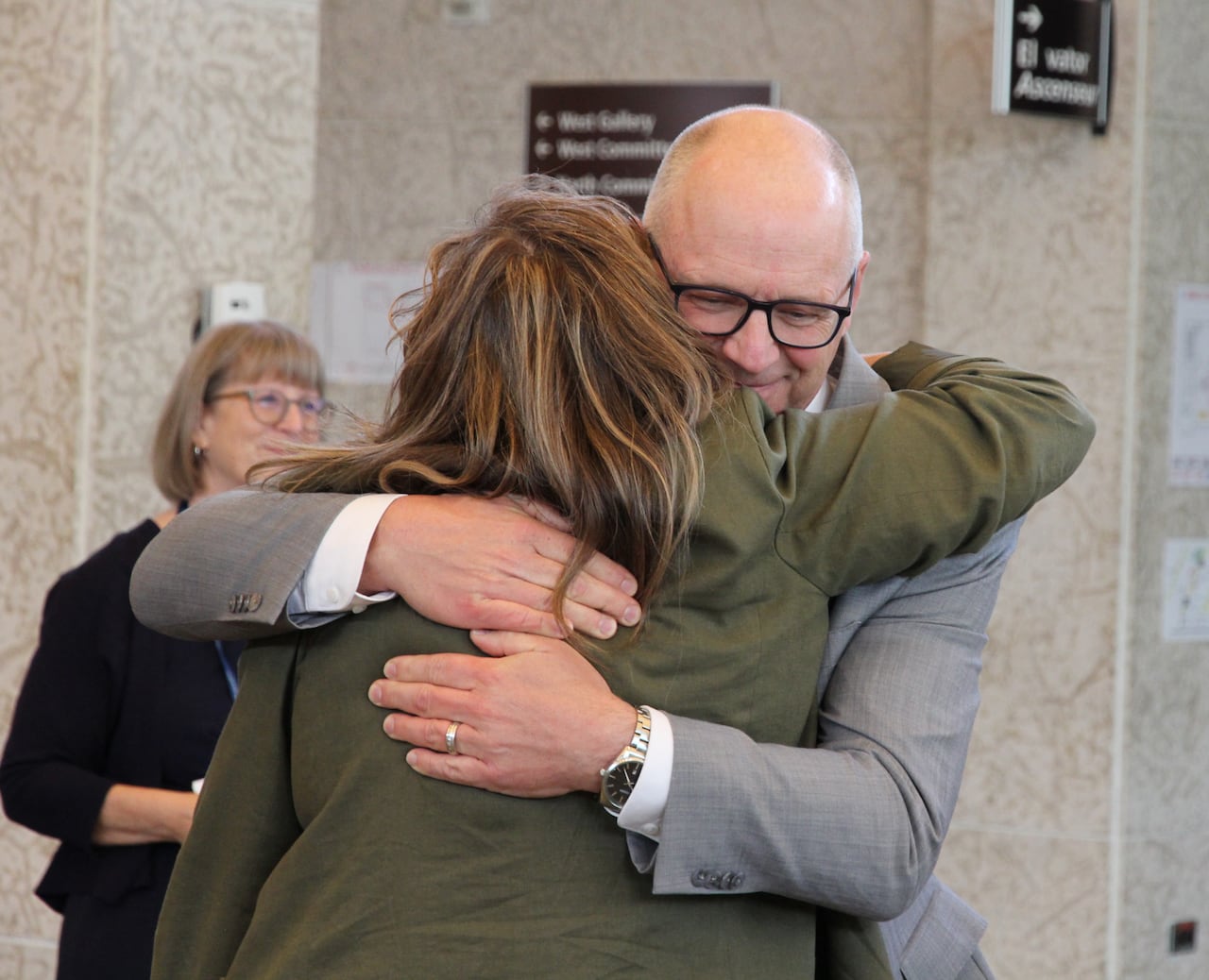A man wearing a grey suit and a woman wearing a green jacket hug each other.