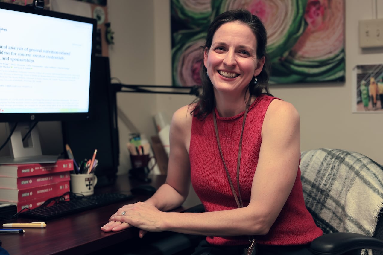 Leah is sitting at her desk and smiling. The study paper being discussed is seen on a computer screen on the desk.