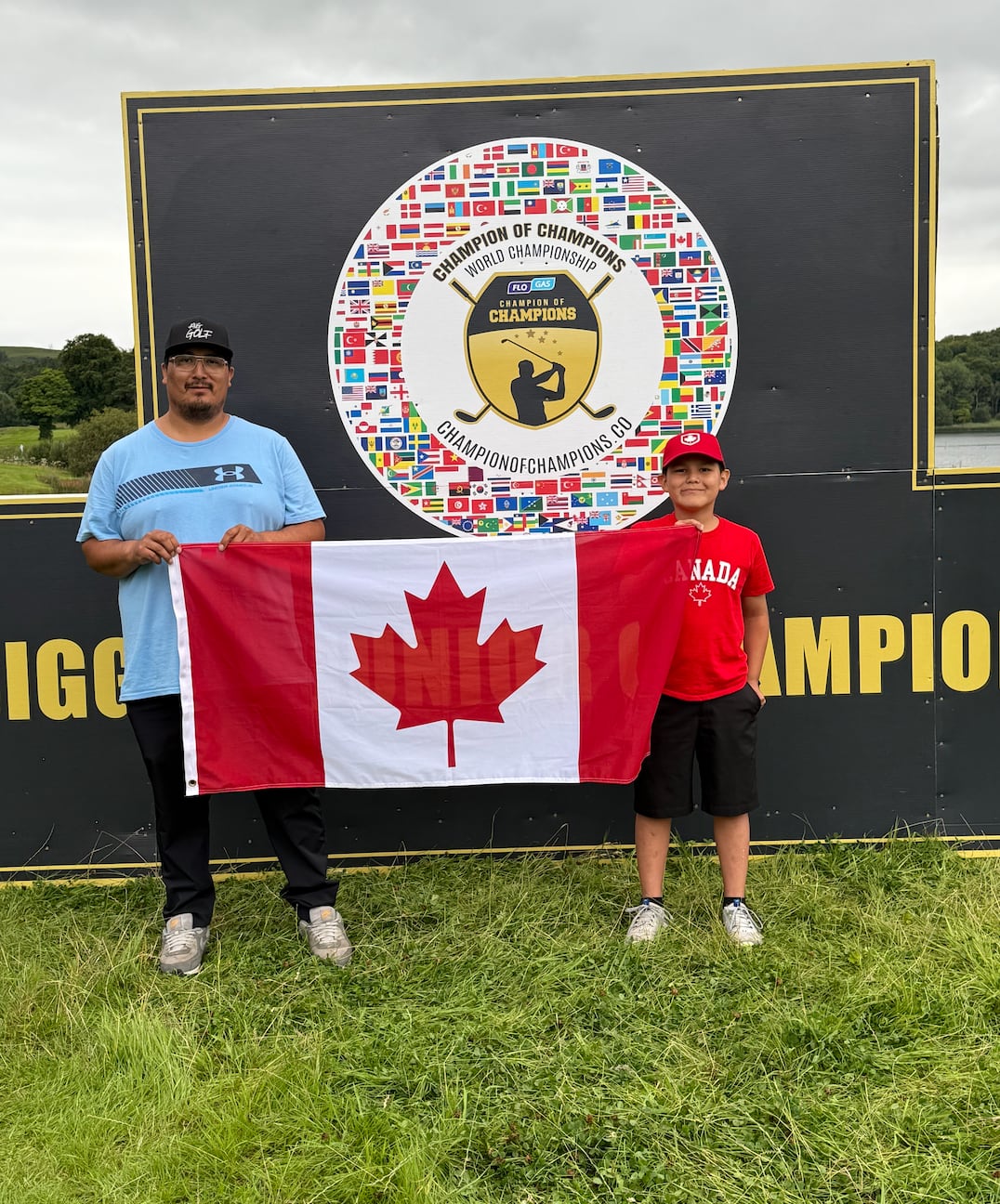 A man and boy stand at a golf course holding the Canadian flag.