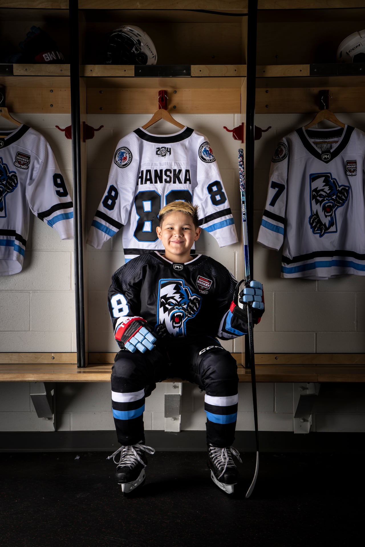 A boy sits in hockey equipment.