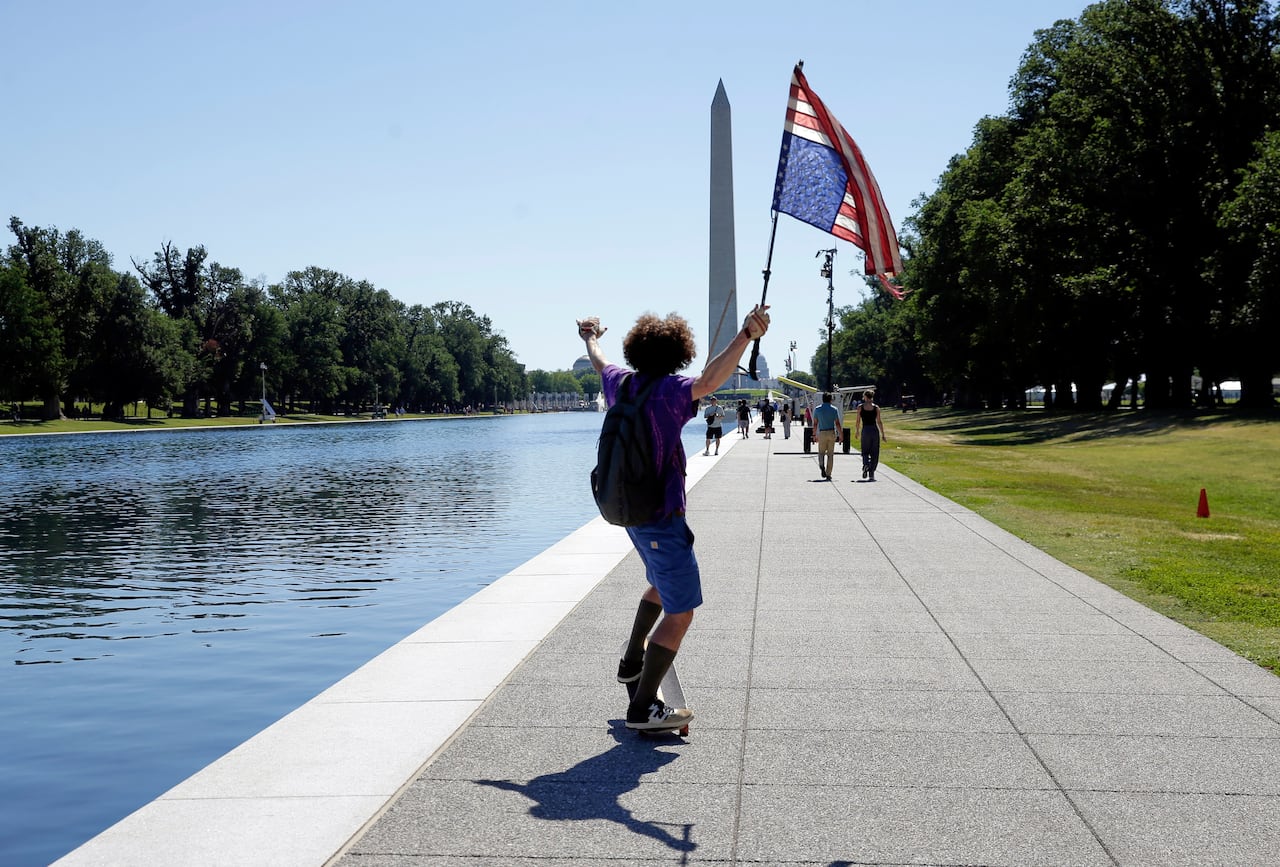 A man skateboards holding an upside-down American flag