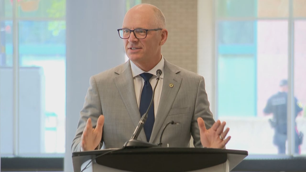 A bald man with glasses wears a suit and speak into a microphone at a podium