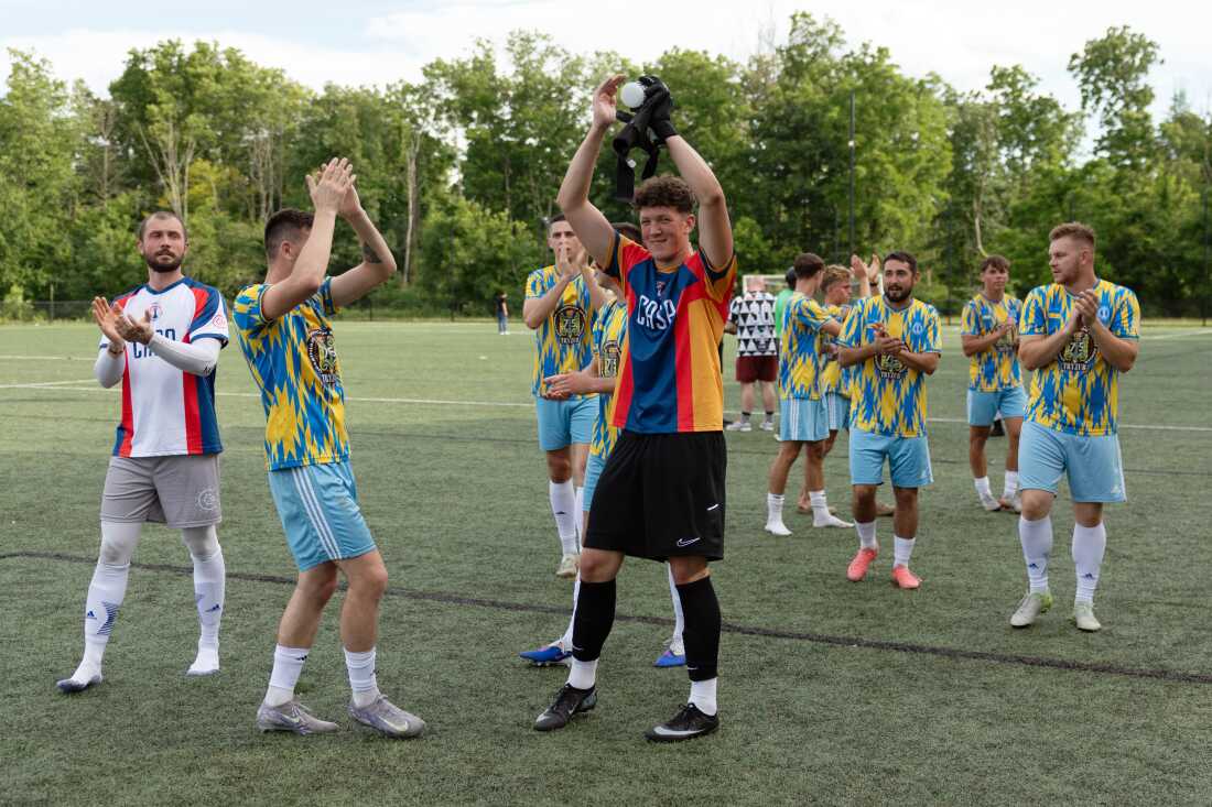 Members of the Philadelphia Ukrainian Nationals soccer team celebrate their win on June 21. Wearing their yellow and light blue soccer uniforms, the members are standing on a green soccer field, clapping and raising their arms in the air.