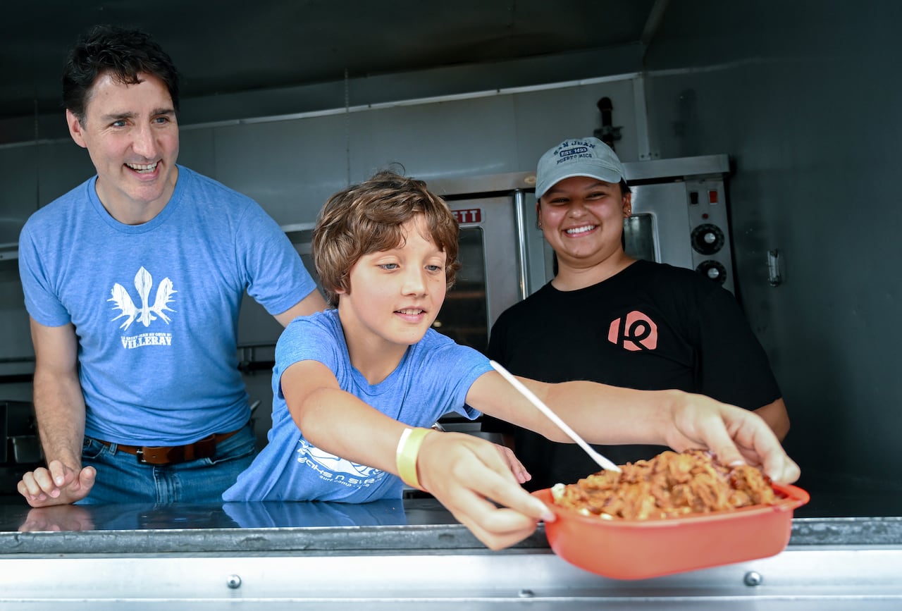 A boy passing out a plate of poutine with a man and a woman next to him.
