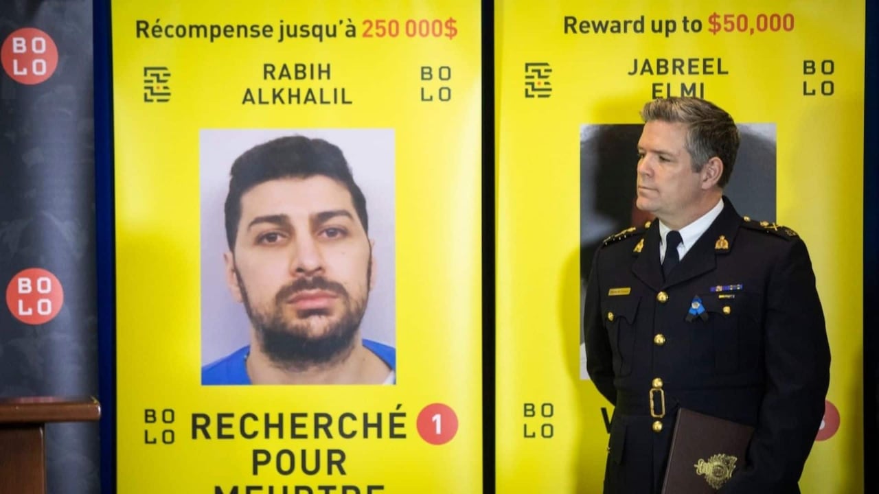 A police officer stands next to a wanted poster with a man's face and a $250,000 reward.