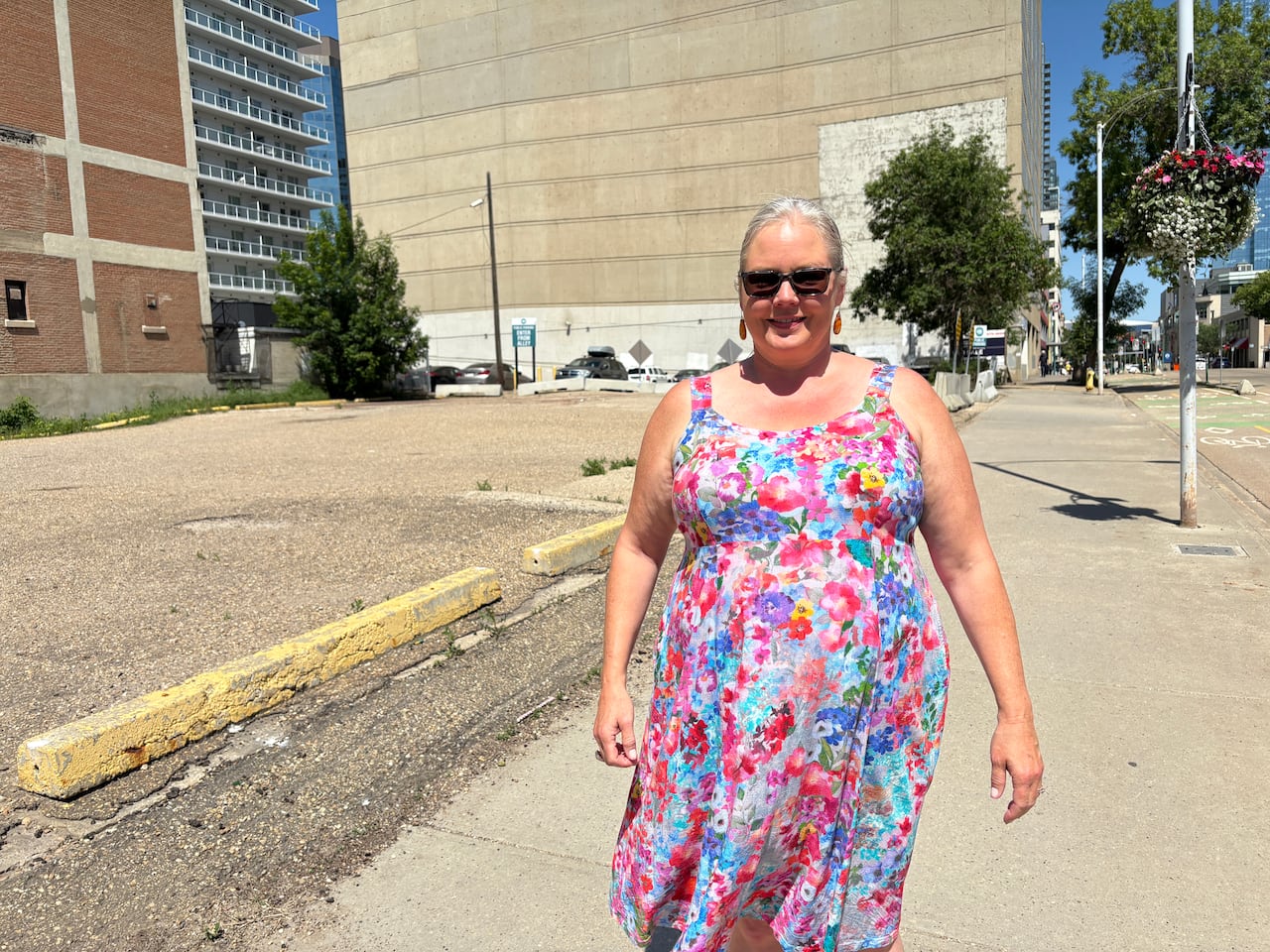 Woman in floral dress next to parking lot.