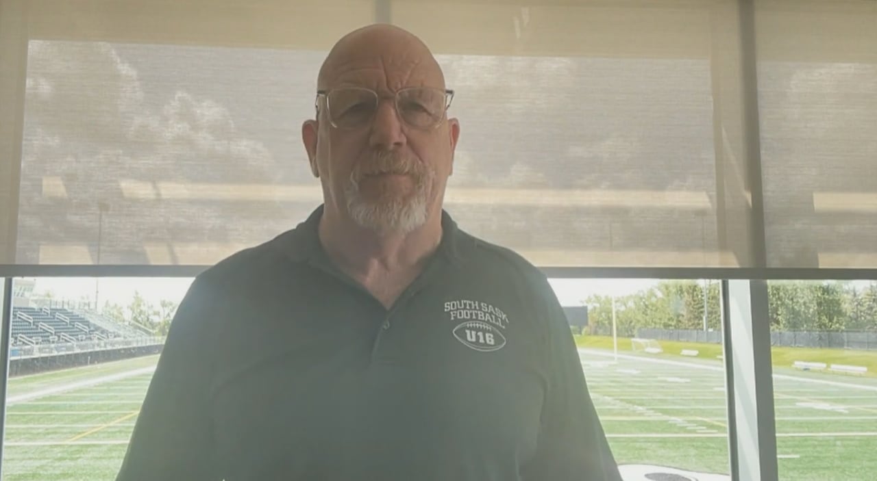 A man stands in front of a window with a football field outside.