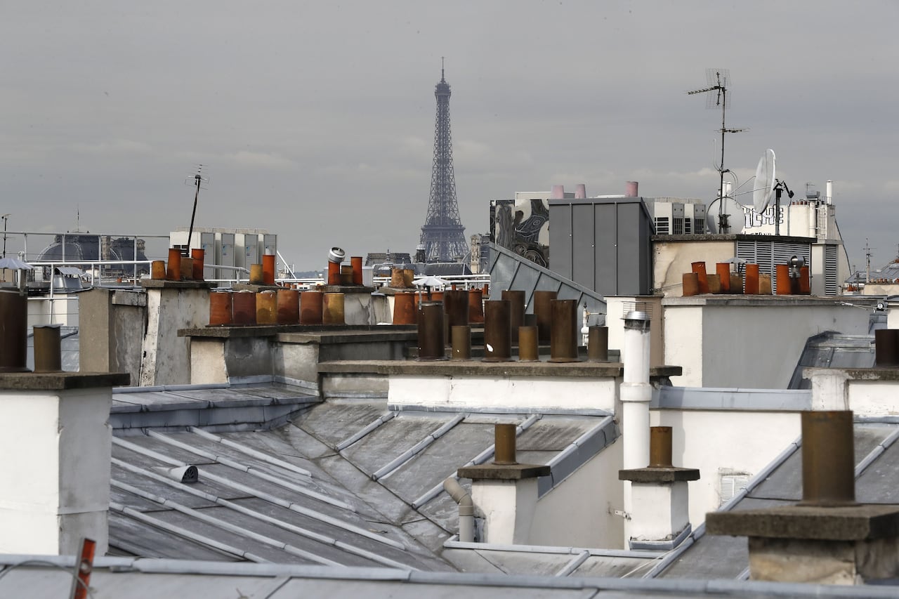 Chimneys among the blue-gray roofs of Paris as the Eiffel tours looms in the background.
