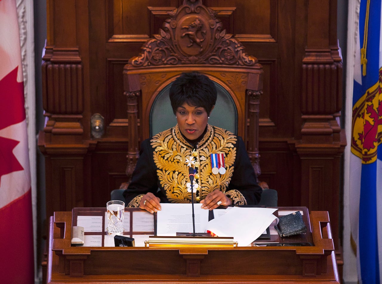 A woman sits at a ceremonial desks and reads from a document.