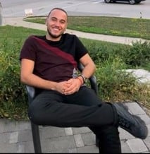 A man sits on a chair outside, smiling.