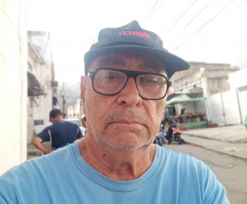 A man in a blue shirt wearing glasses and a hat.