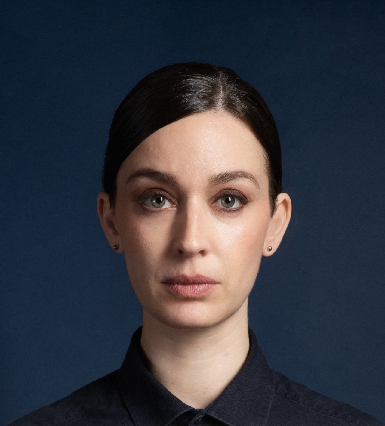 Portrait of a woman with brown hair in a pulled back hairstyle, the artist Dara Vandor. She looks directly at the camera with a neutral expression and the image is composed in the manner of a passport photo.