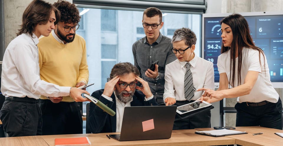 Group of diverse business professionals collaborating in a modern office, analyzing data on laptops and tablets, showcasing teamwork and problem-solving in a corporate environment