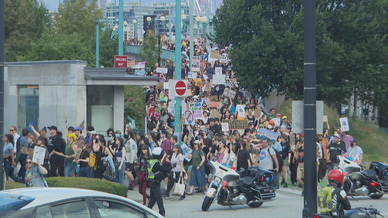 Large crowds of people with protest signs walk down an offramp from a bridge.