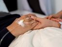 A bedridden patient and another person holding hands.