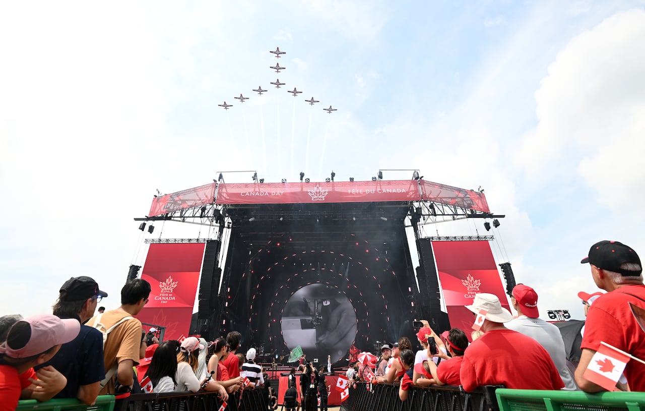 An aerobatic jet team flies in a peace sign formation over a crowd.