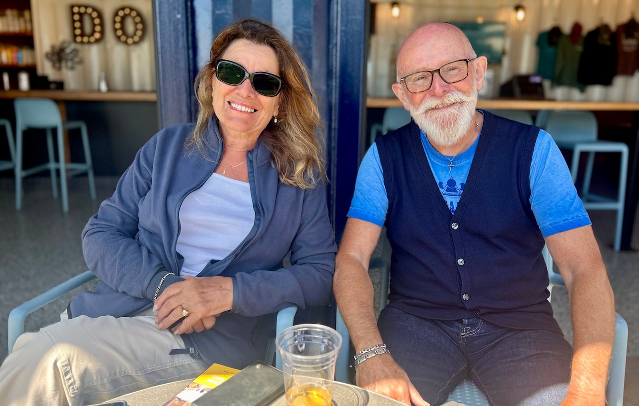 A middle-aged couple sit on a patio with a drink in front of them.