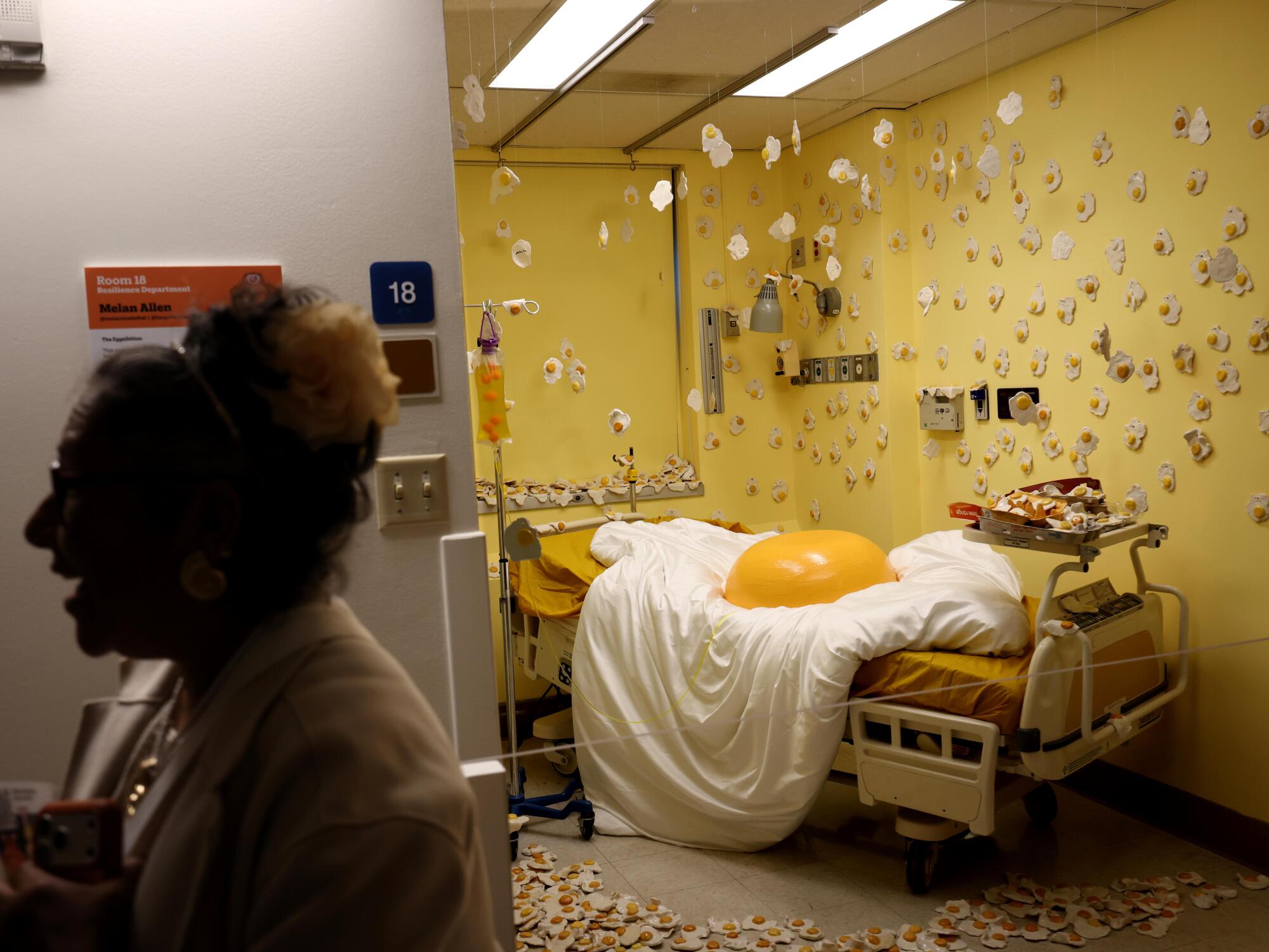 A woman laughs outside a room with a large fried egg on a hospital bed.