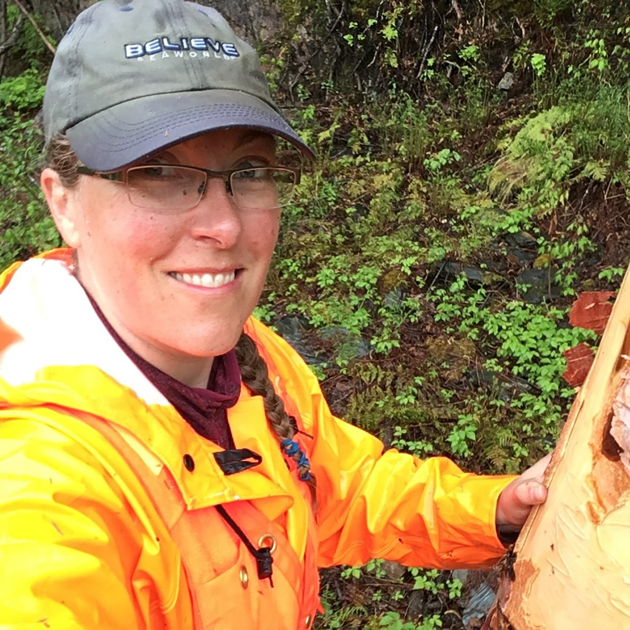A woman with a bright organe rain jacket is seen in a forest.