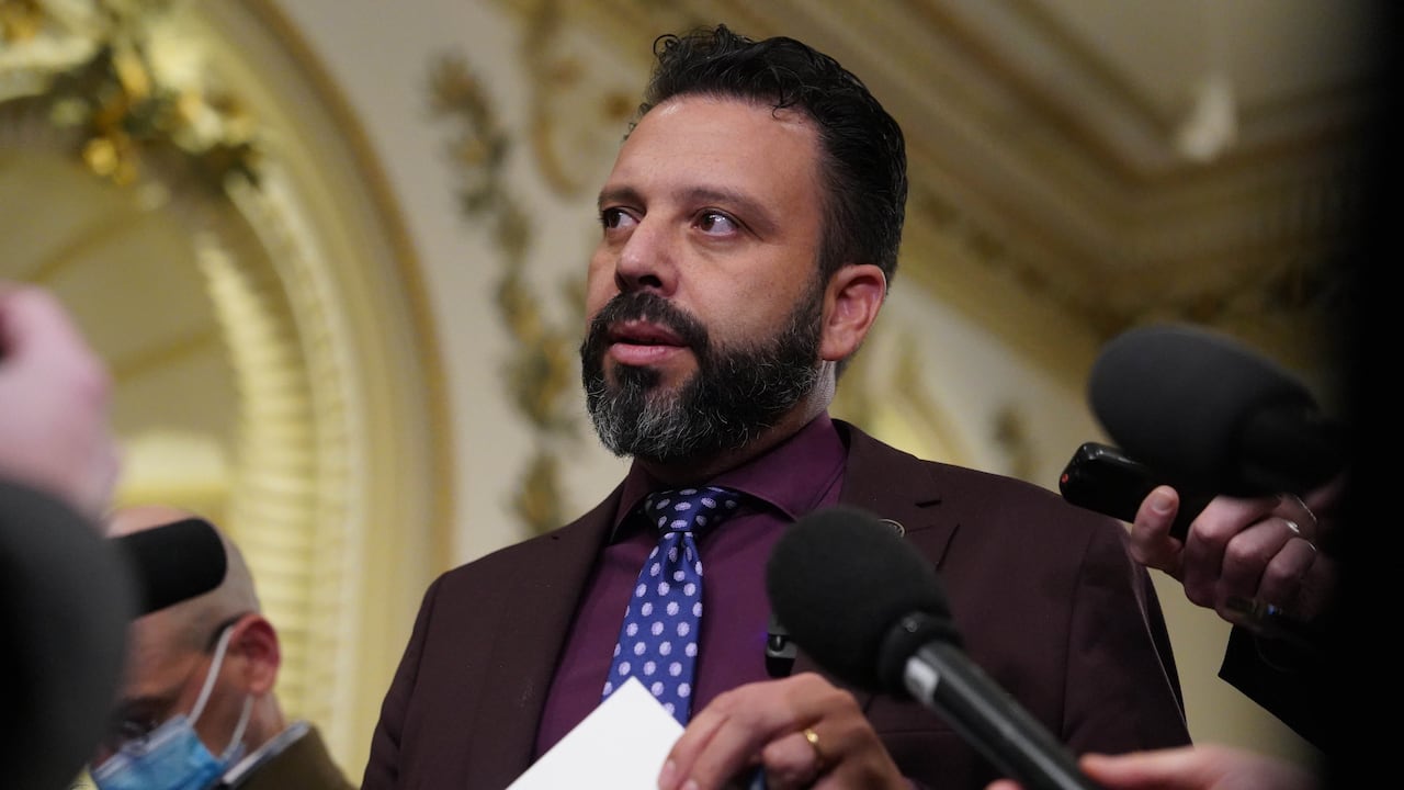 A man in a suit talking into reporters' microphones. 