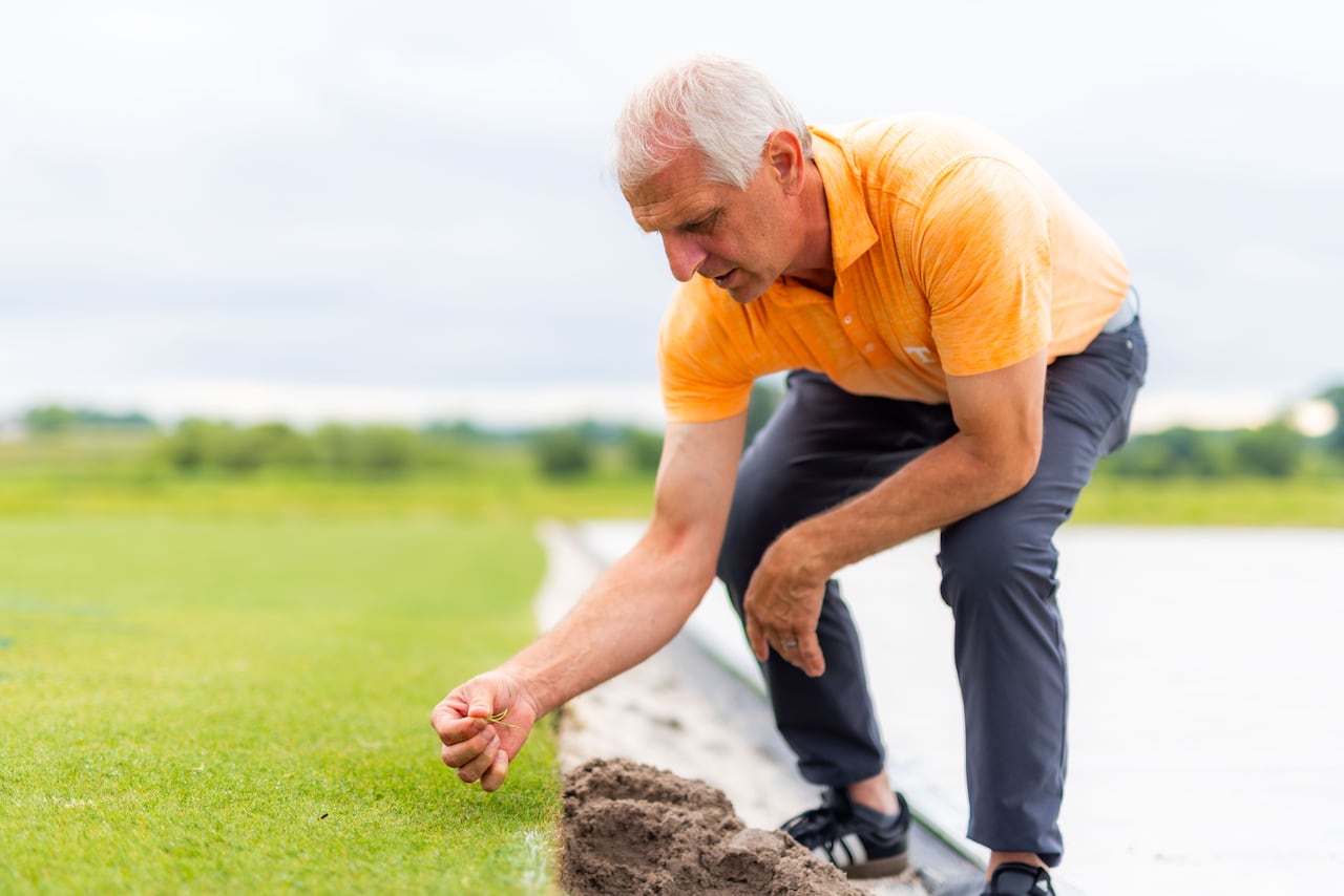 A man reaches down to touch grass.